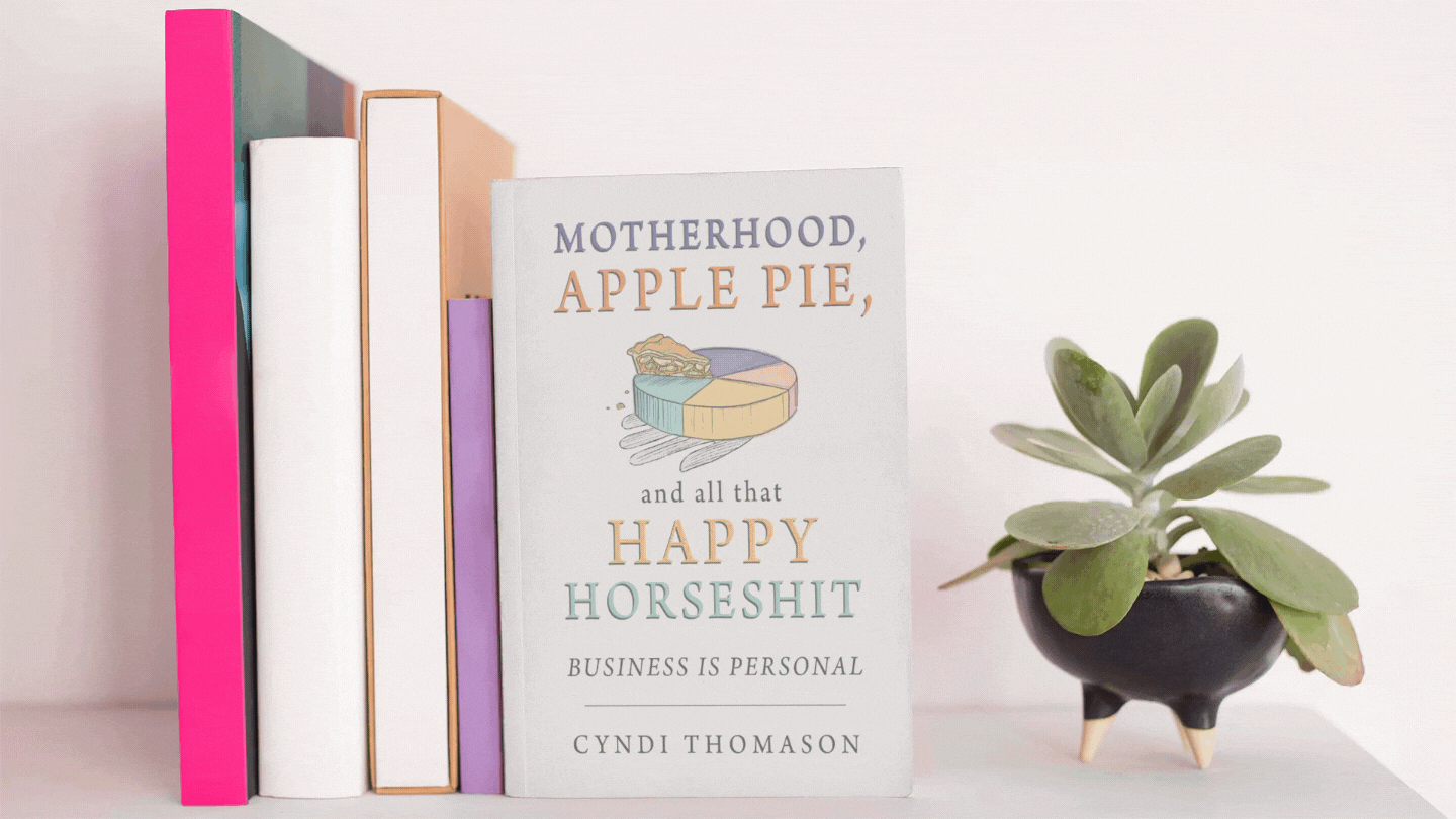 Book shelf displaying Motherhood, Apple Pie, and All That Happy Horseshit book next to a dancing plant.